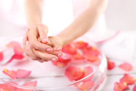 Aromatic bath hand. Treatment hand and nail care women hold hands vial of rose oil over the bowl with rose petalsの写真素材