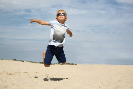 I can fly! The boy jumps up on the sandy beachの写真素材