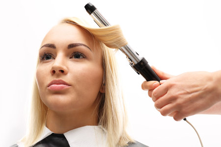 Hairdresser. A woman in a hair salon, barber turns hair curling ironの写真素材