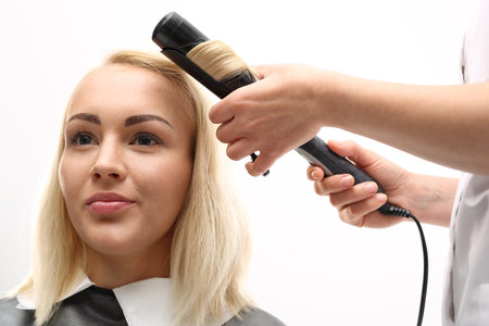 The woman at the hairdresser. A woman in a hair salon, barber turns hair curling ironの写真素材