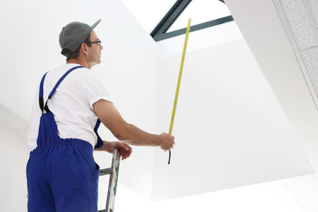 Measurement and man in overalls with a measuring tape standing on a ladderの写真素材