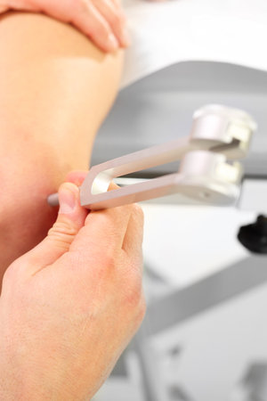 Orthopedic doctor examines the patient's knee using a tuning forkの写真素材