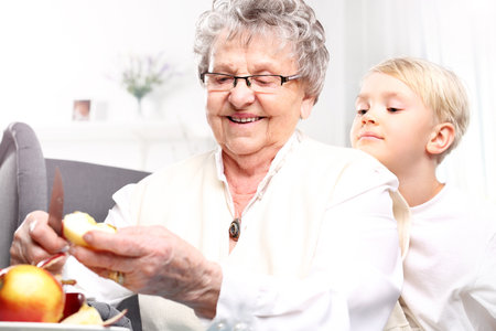 Grandmother looks after the child. Grandmother to grandchild picks an apple peelの写真素材