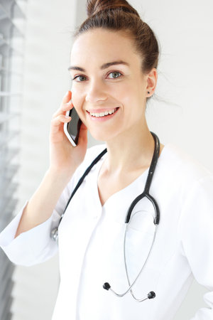 Doctor talking on the phone.The doctor dressed in a white lab coat talking on the phone while standing at the window.の写真素材