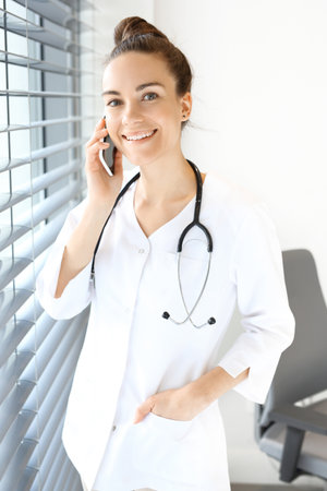 A phone call from the doctor.The doctor dressed in a white lab coat talking on the phone while standing at the window.の写真素材