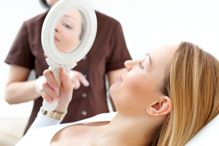 Skin care in the beauty salon. Woman looks in the mirror effect of cosmetic surgery.の写真素材