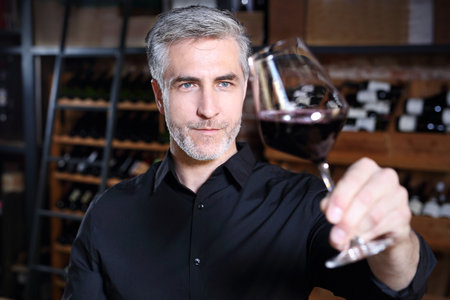 Man poured red wine into a glass. A handsome man judges the color of red wine.の写真素材