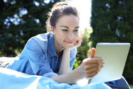 A beautiful young woman relaxing while reading a tablet while sitting on a blanket.の写真素材