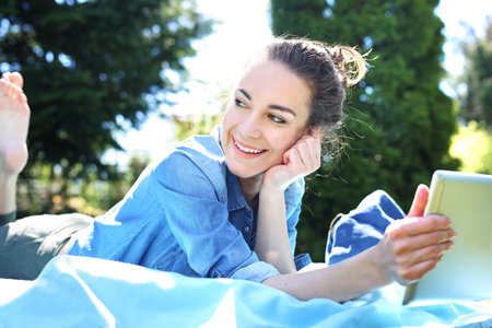 Lazy day. A beautiful young woman relaxing while reading a tablet while sitting on a blanket.の写真素材