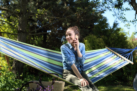 Call.Young attractive woman relaxing on a hammock in the garden talking on the phone.の写真素材
