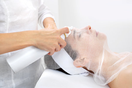 Beautician puts a mask on a woman's face. Woman in a beauty salon during a skin care treatment.