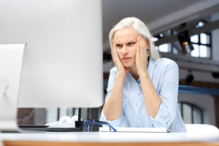 Headache and fatigue at work. Tired woman working at the computer.の写真素材