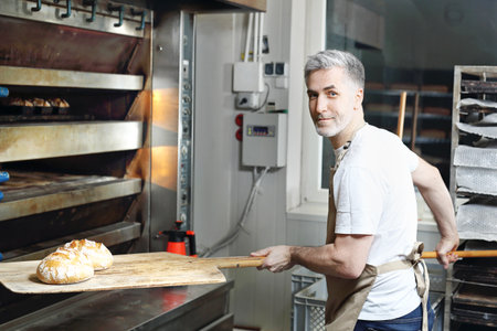 Loaf of bread with golden crust. The baker in the bakery takes out the fresh bread from the ovenの写真素材