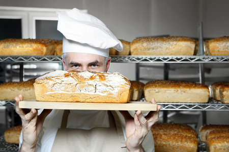 Baking bread. A handsome baker with a loaf of fresh bread.の写真素材