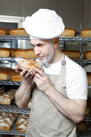 Baker in the bakery. A handsome baker with a loaf of fresh bread.の写真素材