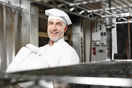 Cheerful baker. Smiling, happy cook carries a sack of flourの写真素材