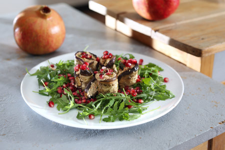 Healthy diet. Eggplant roulades with cheese served with pomegranate on rocket lettuce.の写真素材