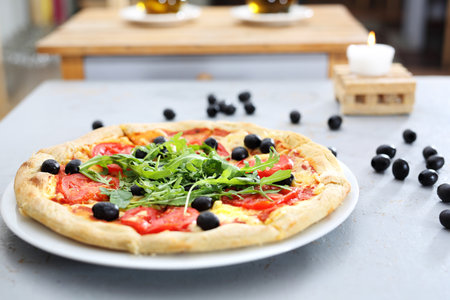 Thin-crust pizza with toppings. Pizza with tomatoes, black olives, arugula.の写真素材