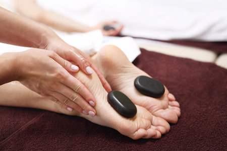 Hot stones massage. Female feet with basalt stones, relaxing in the spa salon.の写真素材