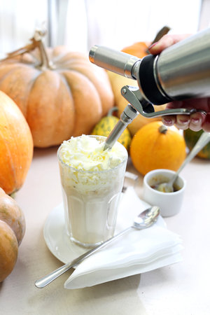 Autumnal coffee dessert. Tasty coffee with milk and whipped cream on the background of autumn pumpkins.の写真素材