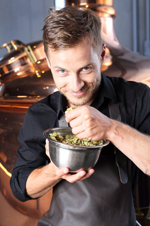 Brewer. Handsome man stands in front of a glass of beer and ingredients for the traditional beer hops and barley maltの写真素材