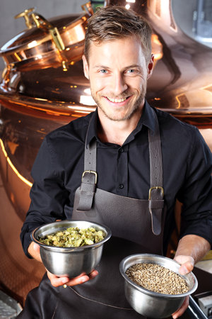 Brewer. Handsome man stands in front of a glass of beer and ingredients for the traditional beer...