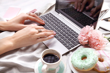 Relax in the morning. A woman writes on the computer while lying on the bed.の写真素材