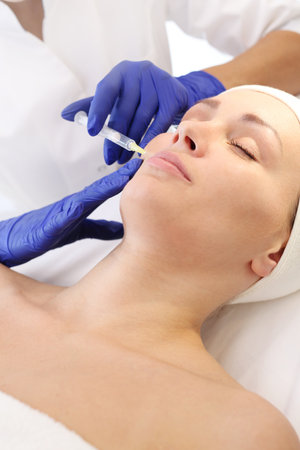 Filling wrinkles with hyaluronic acid. A patient in a cosmetic clinic, a beautician performs an injection procedure.の写真素材