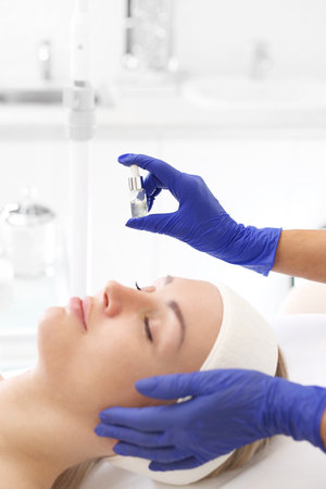 Cosmetic ampoule, a woman in the beauty salon. Beauty imposes on the woman's face cosmetic preparationの写真素材