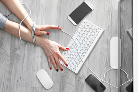 Dependence on new technologies. A woman with bound hands writes on a computer keyboard.の写真素材