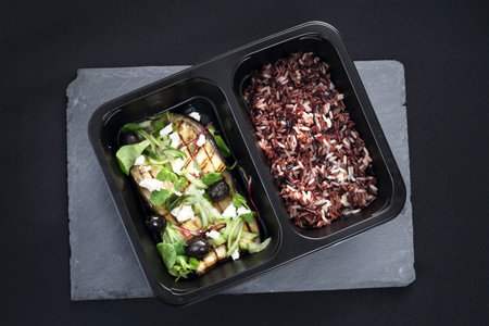 Grilled eggplant with black olives, feta cheese and green vegetables served with wild rice .Ready take-away dish in a lunch boxの写真素材