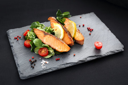 Roasted salmon with salad. Dinner dish on a black plate.の写真素材