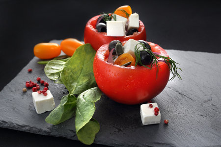 Tomatoes stuffed with olives, feta cheese, spinach served on a black plate.の写真素材