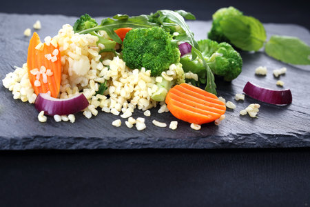 Brown rice with vegetables served on a black plate.の写真素材