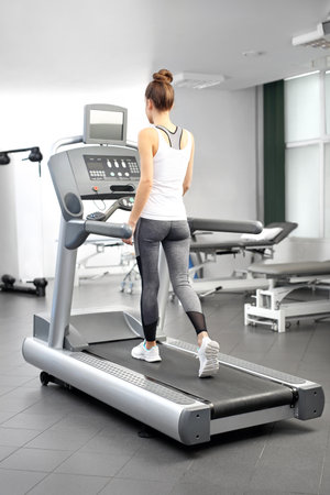 A young woman in an exercise room is running on an automatic treadmill.の写真素材