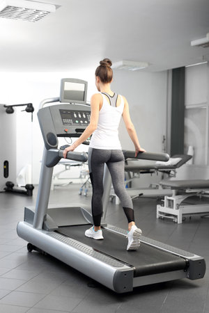 A young woman in an exercise room is running on an automatic treadmill.の写真素材