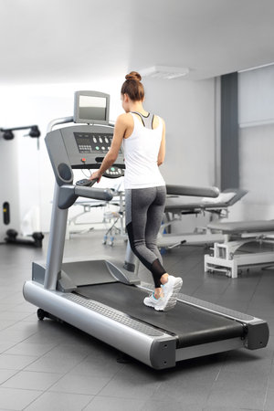 A young woman in an exercise room is running on an automatic treadmill.の写真素材