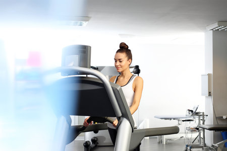 A young woman in an exercise room is running on an automatic treadmill.の写真素材