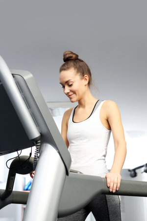 A young woman in an exercise room is running on an automatic treadmill.の写真素材