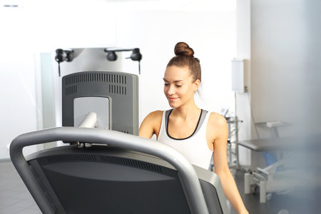 A young woman in an exercise room is running on an automatic treadmill.の写真素材