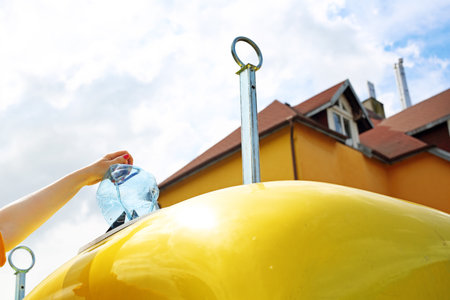Recycling, a woman throws plastic waste into a yellow containerの写真素材