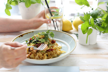 A woman in a restaurant eats pasta. Dish served in the restaurant tagliatelle spaghetti with salmon and dried tomatoes. Proposition of serving the dish.の写真素材