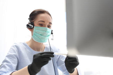 Home office. Sick woman consults doctor's symptoms online. Health protection. A woman in a surgical mask and headphones works at the computer.の写真素材