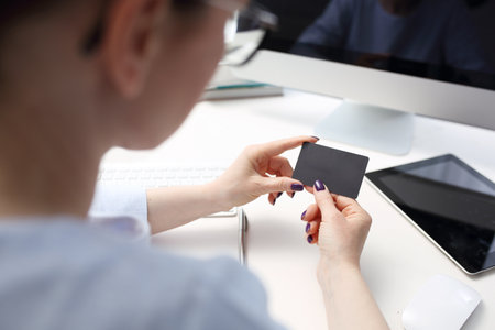 Business card, woman sitting in front of a computer holding a black business card in her hand.の写真素材