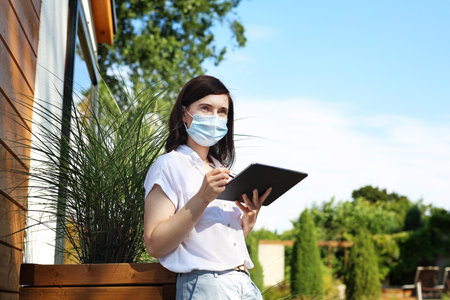 A businesswoman in a protective mask works online. Beautiful young woman writes on a digital tablet. Working outside the office.の写真素材