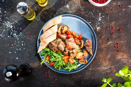 Liver stew with mushrooms and cherry tomatoes, served with bread and fresh salad. The cook cooks and serves an appetizing dish. The finished dish served on a plate. Serving proposal, culinary photograの写真素材