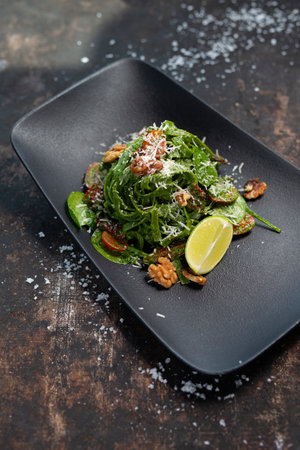 Green spaghetti with spinach, walnuts, cherry tomatoes, and Parmesan cheese. The cook cooks and serves an appetizing dish. The finished dish served on a plate. Serving proposal, culinary photography.の写真素材