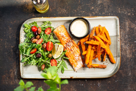 Grilled salmon with sweet potato fries, and salad. The cook cooks and serves an appetizing dish. The finished dish served on a plate. Serving proposal, culinary photography.の写真素材