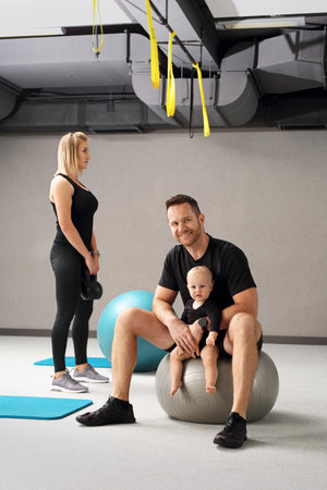 Training with a baby. Mom and dad together in the gym, training with the child in the fitness room.の写真素材