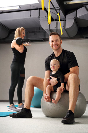 Training with a baby. Mom and dad together in the gym, training with the child in the fitness room.の写真素材